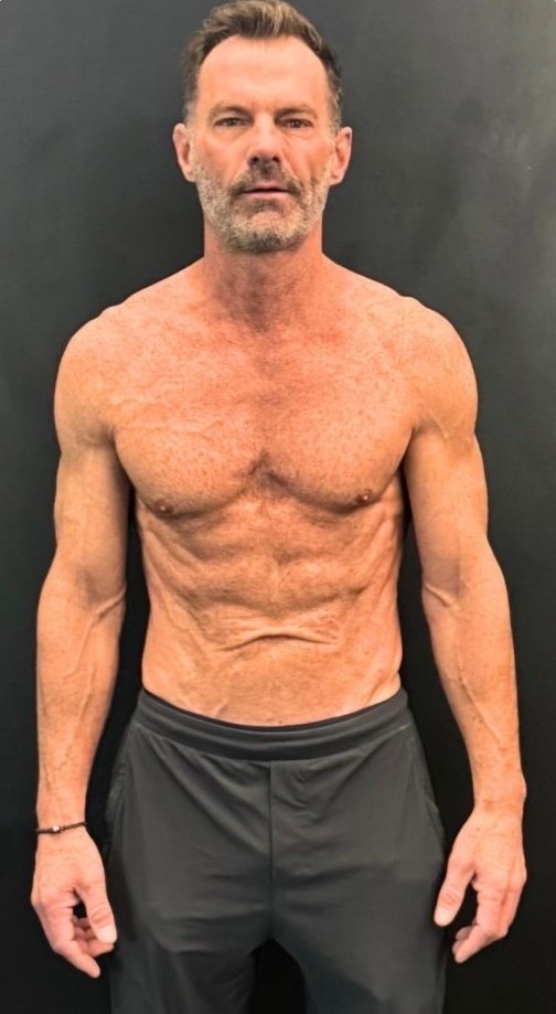 Fit middle aged man standing shirtless against dark background
