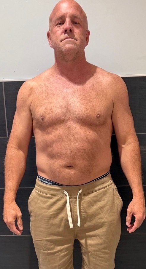 Older man standing shirtless indoors before body transformation