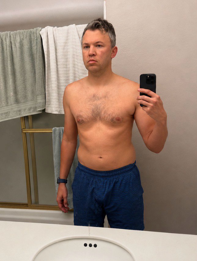 Man taking shirtless bathroom mirror selfie before fitness transformation