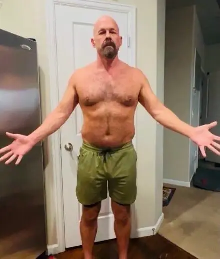 Older man standing shirtless with arms out after fitness transformation