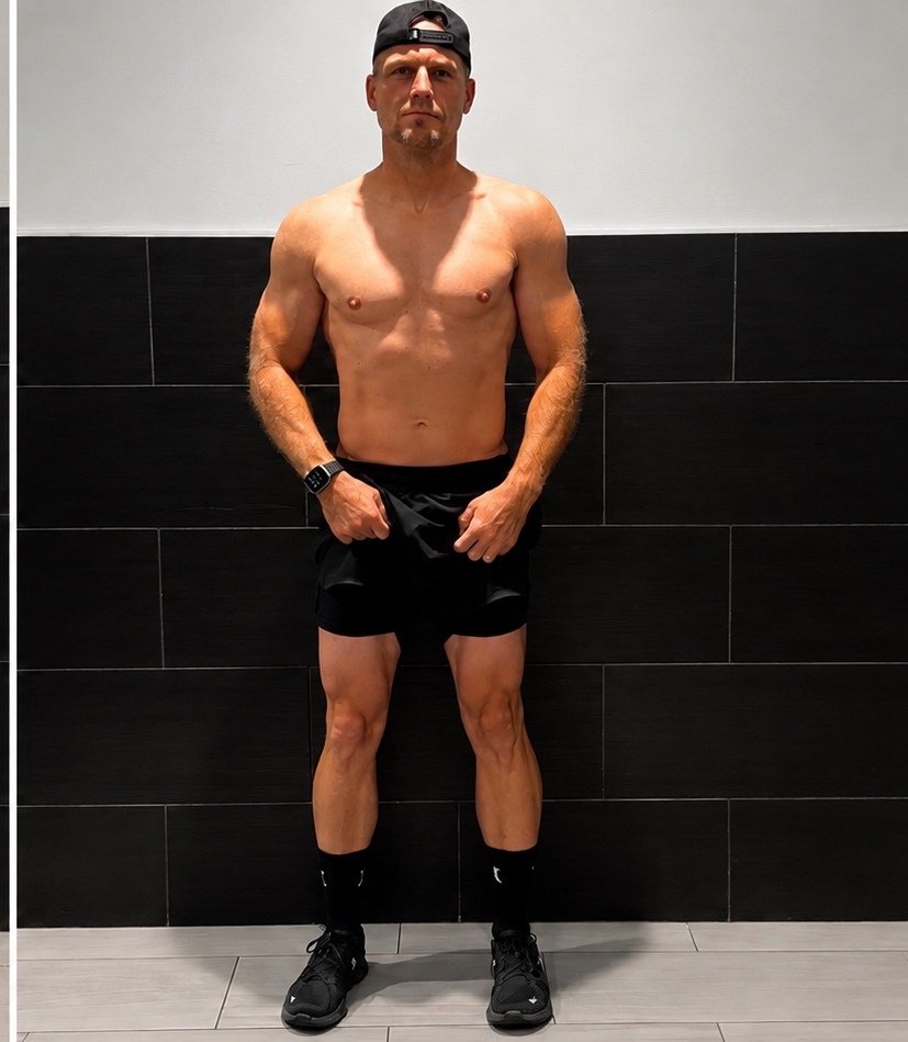 Fit man standing shirtless against black tiled wall in gym
