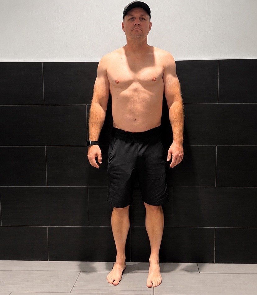 Man standing shirtless against black tiled wall before transformation